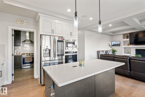 Stainless steel appliances, central kitchen island with countertop, wood-finish flooring, coffered ceiling, and built-in shelving - 824 34 Ave Nw, Edmonton, AB 