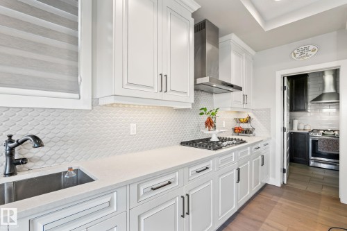 White shaker cabinetry, under-cabinet lighting, stainless steel range hood, stone countertops, and a tile backsplash - 824 34 Ave Nw, Edmonton, AB 