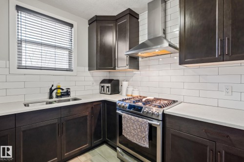 Dark wood-finish cabinetry with silver hardware, white subway tile backsplash, stainless steel range hood, stainless steel gas range, and light-toned countertops - 824 34 Ave Nw, Edmonton, AB 
