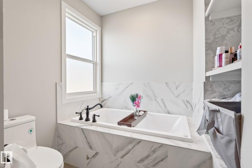 Built-in tub with dark bronze fixtures, framed window, and marble-look tile surround - 824 34 Ave Nw, Edmonton, AB 