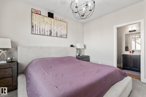 Plush carpeting, contemporary ceiling fan, and access to an ensuite bathroom featuring a vanity with dark wood-finish cabinetry, a single basin, and a wall-mounted light fixture - 824 34 Ave Nw, Edmonton, AB 