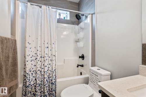 Alcove shower with a white tub and black fixtures, tiled surround, and a fixed window, alongside a toilet and vanity with a light-toned countertop - 824 34 Ave Nw, Edmonton, AB 