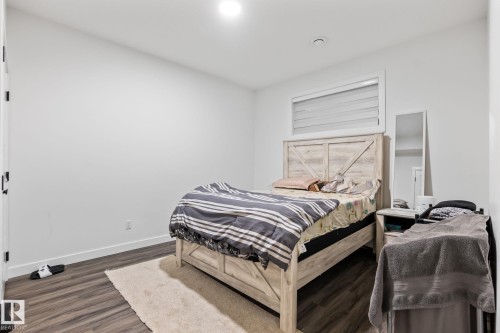 Spacious bedroom featuring wood-finish flooring, a large transom window with plantation shutters, and recessed ceiling lighting - 824 34 Ave Nw, Edmonton, AB 