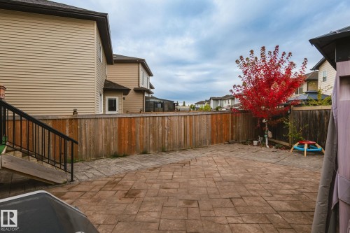 Paved patio area, natural wood fencing, mature tree with red foliage, beige horizontal siding, and a deck with black metal railings - 824 34 Ave Nw, Edmonton, AB 