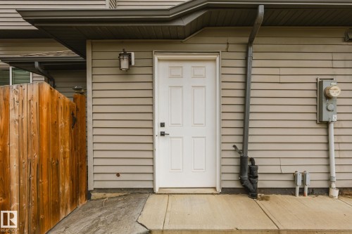 Exterior siding with a white paneled door, featuring a wall-mounted light fixture and wooden fence - 824 34 Ave Nw, Edmonton, AB 
