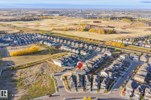 Residential development featuring a mix of detached homes and townhomes, surrounded by undeveloped land and a distant urban landscape - 824 34 Ave Nw, Edmonton, AB 