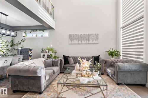 Double-height ceiling, upper-level interior balcony, large vertical window with blinds, and a linear chandelier - 824 34 Ave Nw, Edmonton, AB 