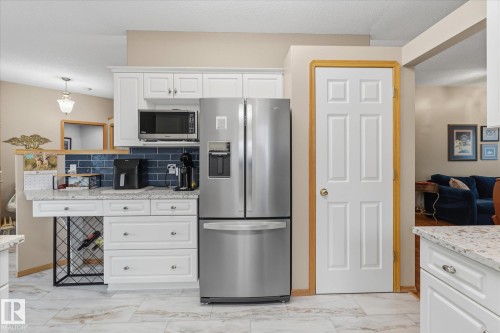 White cabinetry with chrome hardware, subway tile backsplash, stainless steel refrigerator, and wood-finish flooring - 7 Linkside Pl, Spruce Grove, AB 