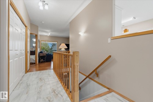 Hallway featuring tile flooring, bi-fold closet doors, wood handrail, and wall sconce lighting - 7 Linkside Pl, Spruce Grove, AB 
