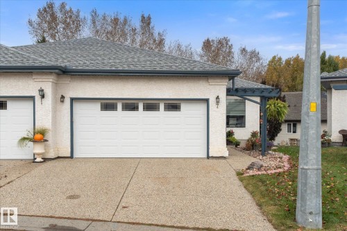 Stucco exterior with a shingle roof, attached garage with panel doors and transom-style windows, and an exposed aggregate driveway - 7 Linkside Pl, Spruce Grove, AB 
