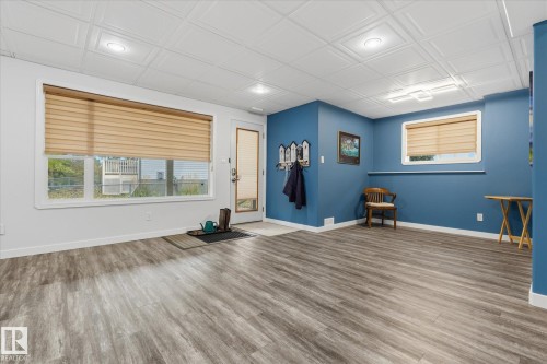 Spacious room featuring wood-finish flooring, a large multi-pane window, white trim throughout, and a textured drop ceiling with recessed lighting - 7 Linkside Pl, Spruce Grove, AB 
