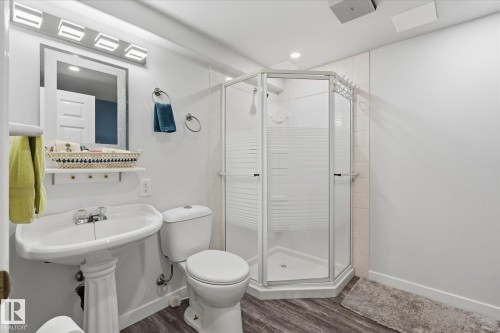 Pedestal sink, wall-mounted mirror with integrated lighting, stand-up shower with frosted glass, wood-finish flooring, and recessed ceiling lighting - 7 Linkside Pl, Spruce Grove, AB 