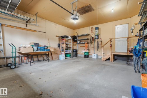 Spacious garage with concrete flooring, overhead garage door system, and an interior access door with a built-in wood platform - 7 Linkside Pl, Spruce Grove, AB 