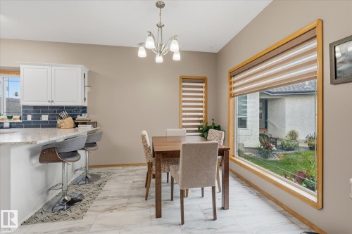 White shaker cabinetry, light-toned backsplash, granite-style countertop, large picture window, and chandelier light fixture - 7 Linkside Pl, Spruce Grove, AB 