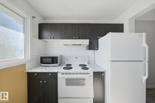 Kitchen featuring dark wood-finish cabinetry, white subway tile backsplash, light-colored countertops, white refrigerator, and white range - 164 Dickinsfield Court Nw, Edmonton, AB 