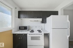 Kitchen featuring dark wood-finish cabinetry, white subway tile backsplash, light-colored countertops, white refrigerator, and white range - 