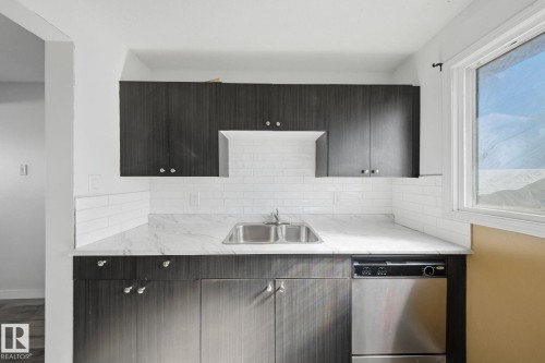 Dark wood-finish cabinetry with silver hardware, white subway tile backsplash, white marble-look countertop, and a stainless steel double-basin sink - 164 Dickinsfield Court Nw, Edmonton, AB 