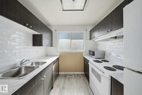 Galley kitchen featuring dark wood-finish cabinetry, white subway tile backsplash, and light-toned countertops - 164 Dickinsfield Court Nw, Edmonton, AB 