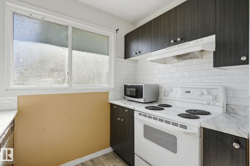 White subway tile backsplash, dark wood-finish cabinetry, white range, and a white window frame - 164 Dickinsfield Court Nw, Edmonton, AB 