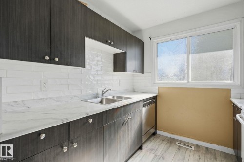 Dark wood-finish cabinetry, white subway tile backsplash, light-toned countertops, and wood-finish flooring - 164 Dickinsfield Court Nw, Edmonton, AB 