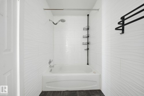 White subway tile surround with textured accent, integrated bathtub, and dark wood-finish flooring - 164 Dickinsfield Court Nw, Edmonton, AB 
