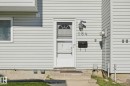 White vinyl siding exterior with an entry door featuring a storm door, an exterior wall lantern, a wall-mounted mailbox, and concrete steps - 164 Dickinsfield Court Nw, Edmonton, AB 