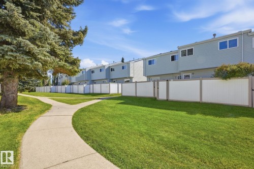 Spacious green space featuring a concrete pathway, mature trees, and a privacy fence - 164 Dickinsfield Court Nw, Edmonton, AB 