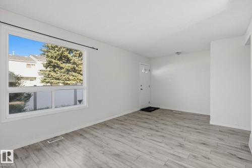 Spacious room with wood-finish flooring, a large window, a white entry door with decorative glass, and a ceiling-mounted light fixture - 164 Dickinsfield Court Nw, Edmonton, AB 