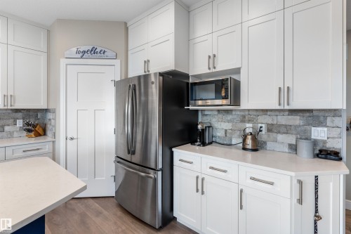 White shaker cabinetry, quartz countertops, brick-patterned backsplash, stainless steel refrigerator, and wood-finish flooring - 3334 Parker Loop Sw, Edmonton, AB 