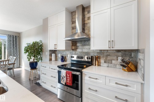 White shaker-style cabinetry, stainless steel range, stainless steel range hood, stone tile backsplash, and light-toned countertops - 3334 Parker Loop Sw, Edmonton, AB 
