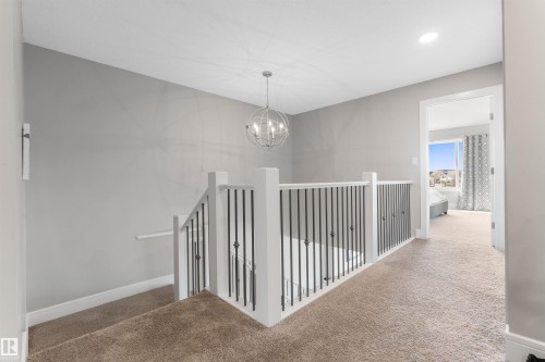 Staircase featuring white newel posts and balusters, dark iron spindles, and brown carpeted treads - 3334 Parker Loop Sw, Edmonton, AB 