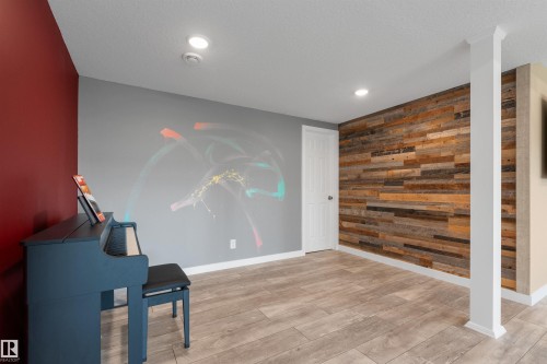 Wood-finish flooring, accent wall with wood paneling, LED lighting, white interior door, and a structural column - 3334 Parker Loop Sw, Edmonton, AB 