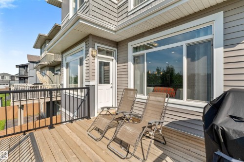 Wood-finish deck with black metal railings, gray horizontal siding, and large pane windows - 3334 Parker Loop Sw, Edmonton, AB 