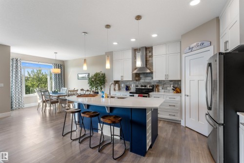 Kitchen featuring a central island with a curved countertop, white cabinetry with contemporary hardware, light wood-finish flooring, recessed lighting, and stainless steel appliances - 3334 Parker Loop Sw, Edmonton, AB 