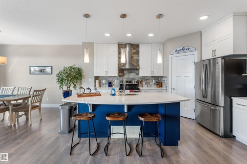 Kitchen featuring an oversized island with a curved countertop, pendant lighting, stainless steel appliances, and wood-finish flooring - 3334 Parker Loop Sw, Edmonton, AB 