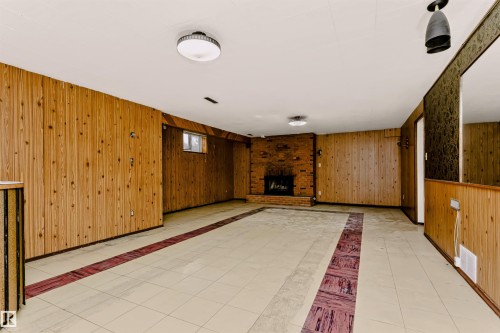 Brick fireplace with a raised hearth, wood paneling, tiled flooring, and multiple ceiling-mounted light fixtures - 11440 44A Avenue Nw, Edmonton, AB 