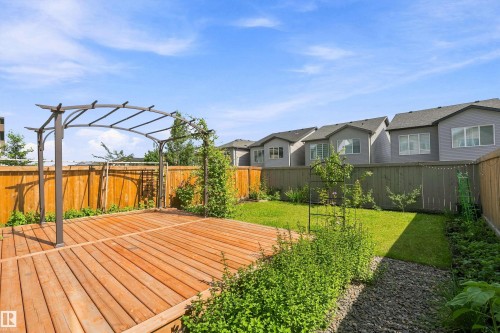 Expansive backyard oasis featuring a composite wood-finish deck with pergola structure, mature landscaping with lush green lawn, and professionally designed hardscape borders - 9227 223 Street Nw, Edmonton, AB 