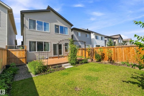 Rear exterior featuring siding, upper and lower windows, a ground-level wood deck, and a fenced yard with lawn - 9227 223 Street Nw, Edmonton, AB 