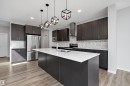 Kitchen featuring wood-finish flooring, dark wood-finish cabinetry, a large kitchen island with a white countertop, stainless steel appliances, and geometric pendant lighting - 9227 223 Street Nw, Edmonton, AB 