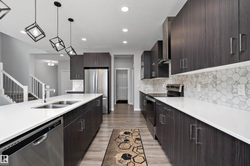 Kitchen featuring dark wood-finish cabinetry, white countertops, stainless steel appliances, and a hexagonal tile backsplash - 9227 223 Street Nw, Edmonton, AB 