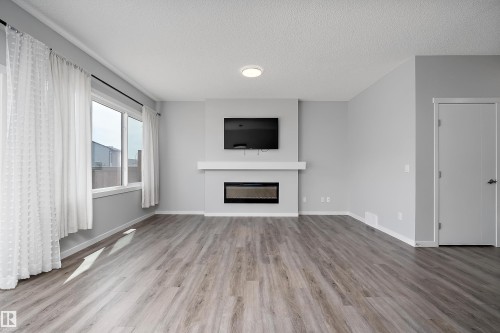Spacious room featuring wood-finish flooring, large windows, a built-in electric fireplace, and light gray walls - 9227 223 Street Nw, Edmonton, AB 