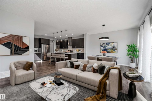 Open-concept living space featuring wood-finish flooring, recessed lighting, dark cabinetry, and an island with seating - 9227 223 Street Nw, Edmonton, AB 