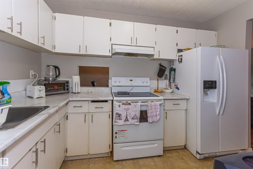 White cabinetry with brushed nickel hardware, white laminate countertops, integrated kitchen sink, white range, and white side-by-side refrigerator - #6 3819 76 St Nw, Edmonton, AB 