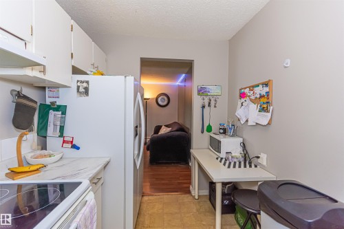 Galley kitchen featuring white cabinetry, light-toned countertops, and a full-size refrigerator - #6 3819 76 St Nw, Edmonton, AB 