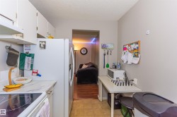 Galley kitchen featuring white cabinetry, light-toned countertops, and a full-size refrigerator - 