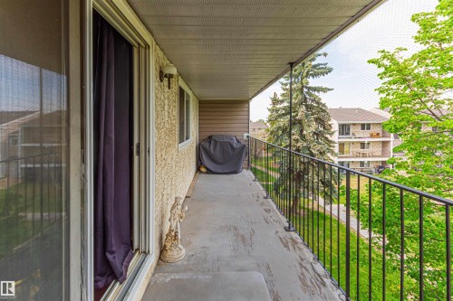 Expansive balcony with concrete flooring, black metal railings, textured exterior wall, and sliding glass door access - #6 3819 76 St Nw, Edmonton, AB 