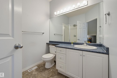 Bathroom featuring a white vanity with panel cabinetry, a blue speckled countertop, an oval undermount sink, a large wall-mounted mirror, and a shower enclosure - 7521 111 Avenue Nw, Edmonton, AB 