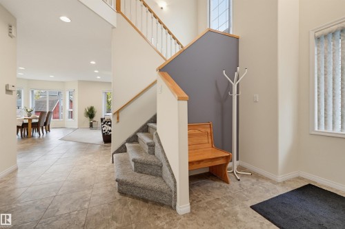 Tiled entryway with a carpeted staircase and wood railing - 7521 111 Avenue Nw, Edmonton, AB 