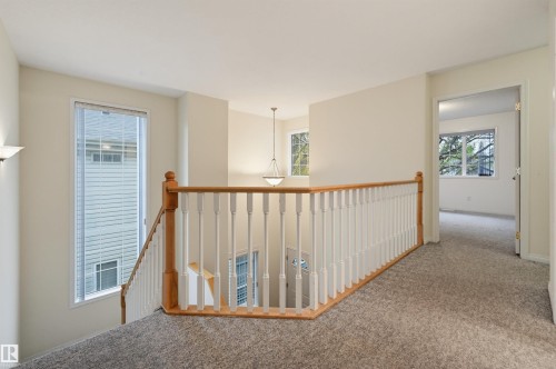 Carpeted hallway with wood banister, white balusters, and a wall-mounted sconce - 7521 111 Avenue Nw, Edmonton, AB 
