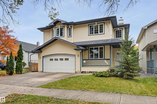 Two-story residence featuring light-colored siding, a covered front porch with a railing, an attached garage, and a concrete driveway - 7521 111 Avenue Nw, Edmonton, AB 